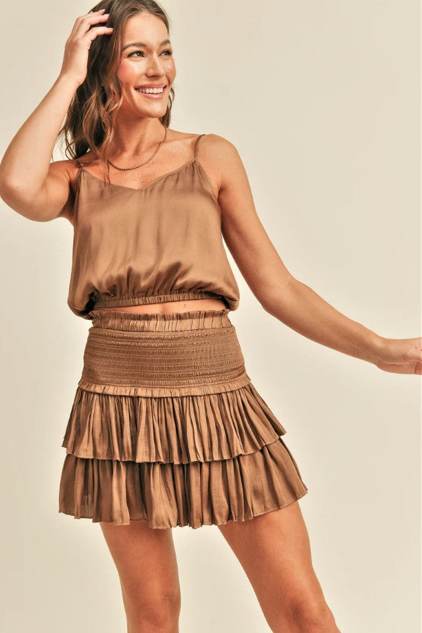 Woman wearing a bronze satin top and skirt on a beige background